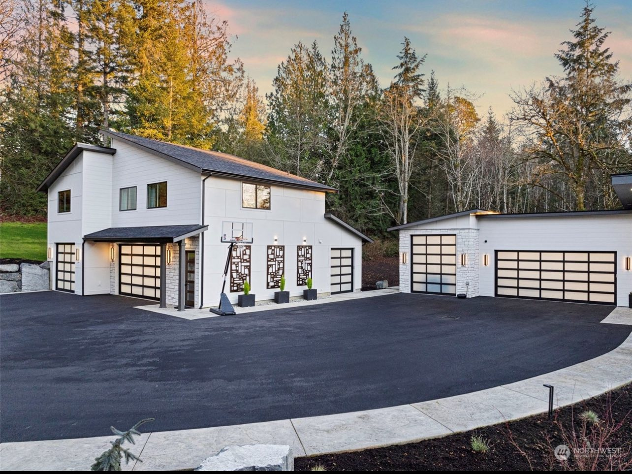 Modern custom estate with glass garage doors and stone accents at dusk in Gig Harbor, WA