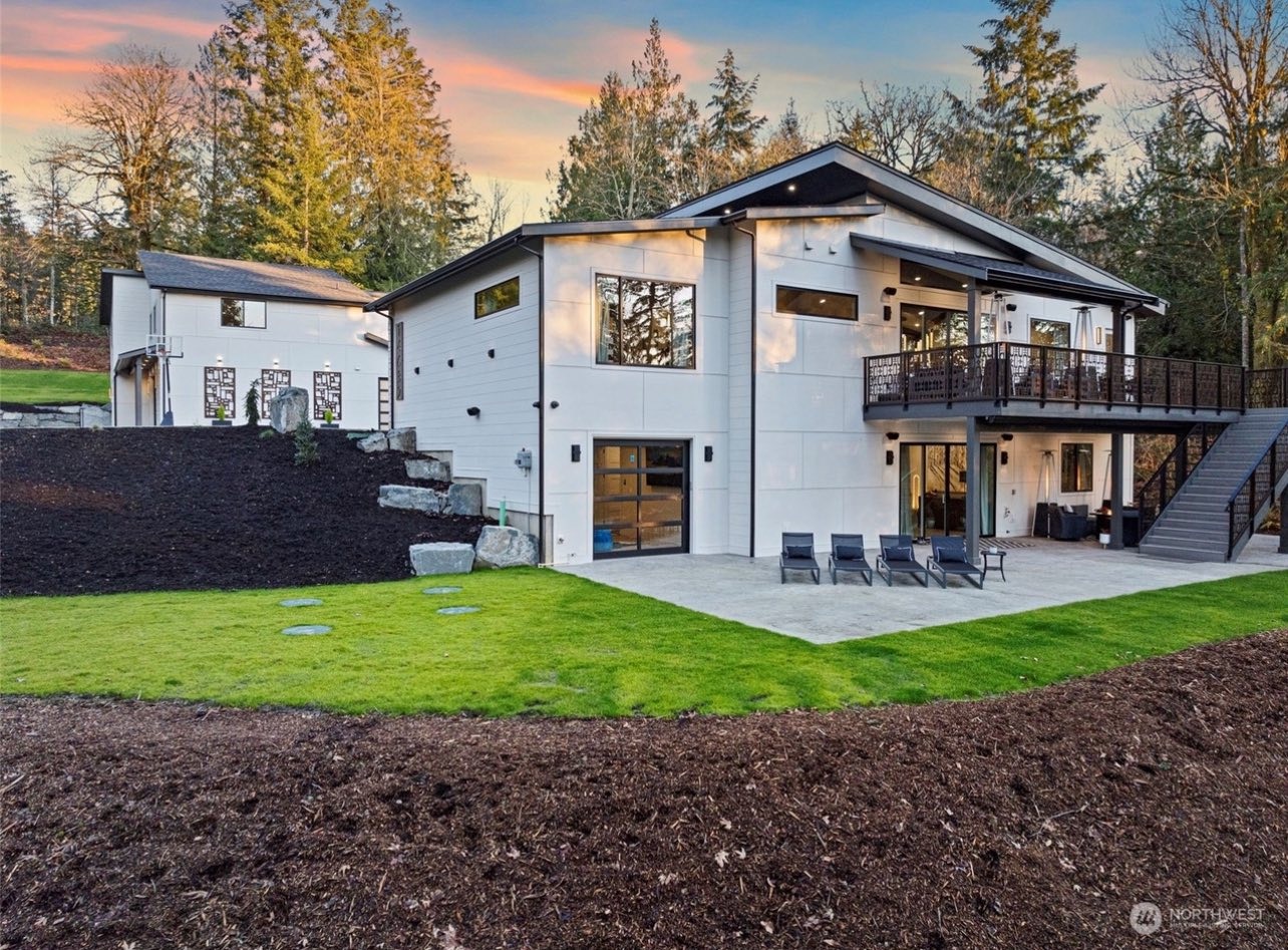 Rear view of modern custom home with landscaped backyard and elevated deck at sunset